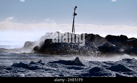 Die Wellen schlagen gegen die eisige Küste des Lake Michigan, wobei bei Temperaturen unter dem Gefrierpunkt Dampf aus dem Wasser kommt. Aufgenommen am Gillson Beach in Wilmette, IL Stockfoto