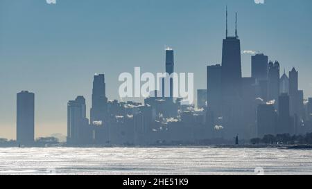 Silhouette der Skyline von Chicago an einem Wintermorgen mit Eisbildung am Lake Michigan im Vordergrund und Dampf, der aus dem Wasser steigt. Stockfoto