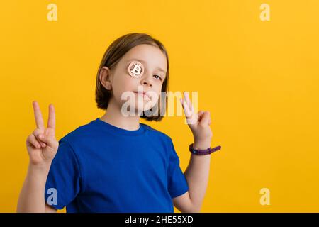 Selbstbewusstes Mädchen 8-10 Jahre alt in Basic Blue T-Shirt mit goldenem physischem Bitcoin auf gelbem Hintergrund. Kinder Finanzielle Kompetenz. Kryptowährung und Blockchain. Spielen, um zu verdienen. Geld verdienen NFT Stockfoto