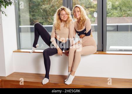 Zwei sportliche junge Frauen, die sich nach dem Pilates-Training im Stretching-Studio fröhlich ausruhen. Gesundes Lifestyle-Konzept Stockfoto