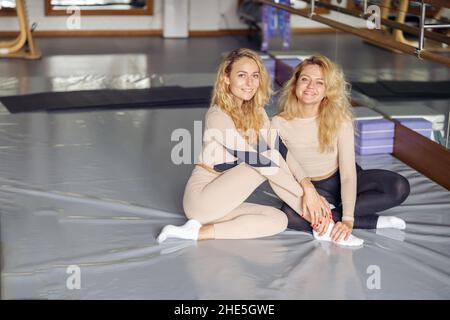 Zwei reizende junge, fit Frauen lächeln vor der Kamera, während sie nach dem Pilates-Training im Stretching-Studio zusammen posieren. Aktives und gesundes Lifestyle-Konzept Stockfoto