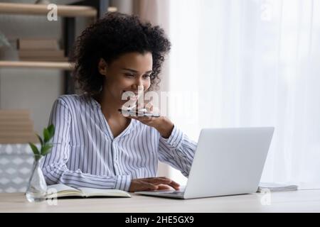 Glückliche junge afroamerikanische Geschäftsfrau, die im Büro eine Audiobotschaft aufzeichnete. Stockfoto