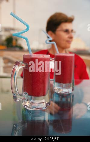 Gläser mit frischem Granatapfelsaft und älterer Frau im Hintergrund Stockfoto