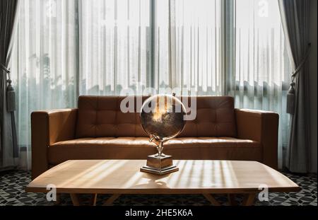 Chiang Rai, Thailand - Sep 06, 2020 : Replik Globus auf Holz Couchtisch vorne zu braunem Ledersofa auf Hintergrund der weißen Vorhänge im Wohnzimmer w Stockfoto