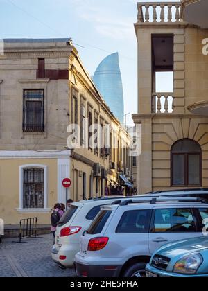 Baku, Aserbaidschan - 5. Mai 2019: Alte Architektur von Baku mit geparkten Autos und Fußgängern, die an einem warmen Frühlingstag zu Fuß gehen, und den ikonischen Flame Towers, einem Trio von Wolkenkratzern im Hintergrund Stockfoto