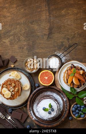 Wir feiern den Pfannkuchen-Tag, ein gesundes Frühstück. Köstliche hausgemachte amerikanische Bananen-Pfannkuchen mit Heidelbeeren, Nüssen, Karamell, Schokolade, roter Orange auf rus Stockfoto