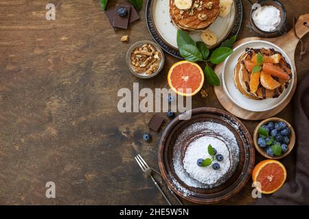 Wir feiern den Pfannkuchen-Tag, ein gesundes Frühstück. Köstliche hausgemachte amerikanische Bananen-Pfannkuchen mit Heidelbeeren, Nüssen, Karamell, Schokolade, roter Orange auf rus Stockfoto