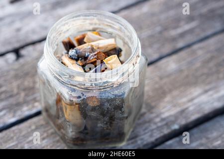 Nahaufnahme von vielen geräucherten Zigarettenkippen in einer Flasche auf einem Holztisch Stockfoto