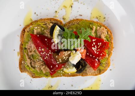 Teller mit Sandwich aus der Dose mit Thunfisch, Guacamole, Pfeffer, Tomaten, Oliven, Rucola und Feta-Käse Stockfoto