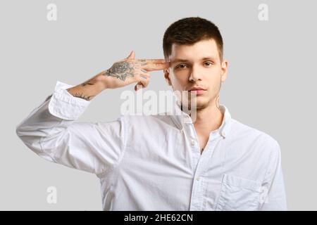 Der junge Mann legte seinen Zeigefinger über grauem Hintergrund auf seinen Tempel Stockfoto