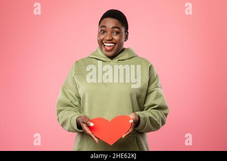 Happy Oversized African Lady Zeigt Rotes Papierherz, Studioaufnahme Stockfoto