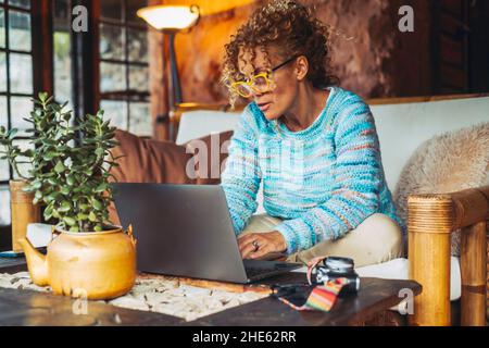 Moderne nette Frau Erwachsene mittleren Alters arbeiten zu Hause mit Laptop-Computer auf der Couch sitzen - Technologie online Menschen Lifestyle-Konzept - Erwachsene fema Stockfoto
