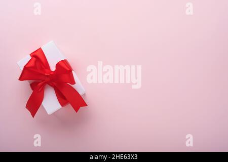 Weiße Geschenkschachteln mit rotem Band und kleinen roten Zierherzen auf rosa Hintergrund. Draufsicht mit Kopierbereich. Valentinstag oder Hochzeit romantisch konz Stockfoto