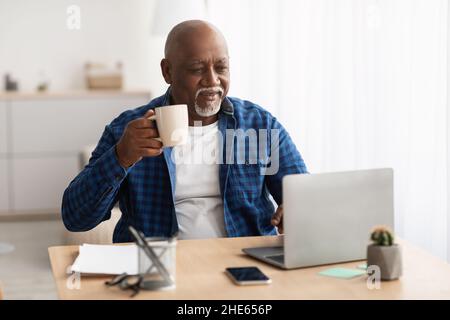 Schwarzer Reifer Mann Arbeitet Auf Laptop Kaffee Trinken Am Arbeitsplatz Stockfoto