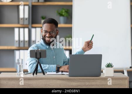 Freundlich fröhlich tausendjährigen afroamerikanischen Mann Tutor zeigen, um englische Regeln, schaut auf pc und Smartphone Webcam Stockfoto