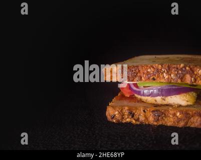 Gegrilltes Sandwich mit Tomaten, Zwiebeln, Huhn, Salat und Mehrkornbrot. Nahaufnahme mit Kopierraum und dunklem Hintergrund. Stockfoto