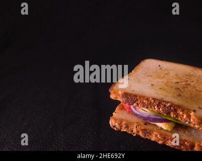 Gegrilltes Sandwich mit Tomaten, Zwiebeln, Huhn, Salat und Mehrkornbrot. Nahaufnahme mit Kopierraum und dunklem Hintergrund. Stockfoto