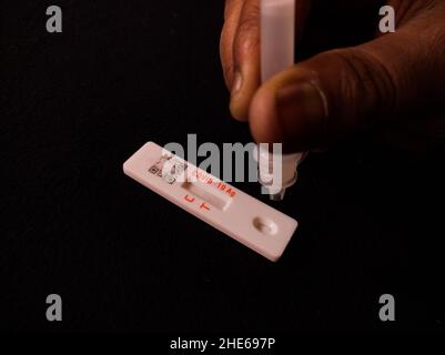 covid19 oder neuartiger Coronavirus-omicron-Test in der Schnellantigen-Methode. Tropfen extrahierter Antigenlösung von Hand auf Selbsttest-Kit. Schuss im Dunkeln Stockfoto