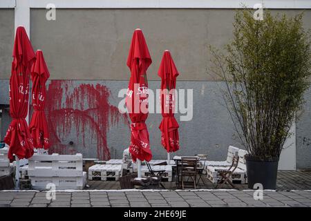 Weiße Bistromöbel aus Europaletten und rote Schirme eines geschlossenen Bistro im Freien während der Corona-Pandemie. Stockfoto