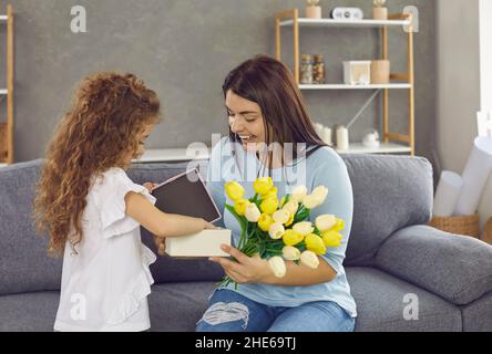 Die kleine Tochter gratuliert ihrer liebenden Mutter im Urlaub mit Geschenken und Blumen. Stockfoto