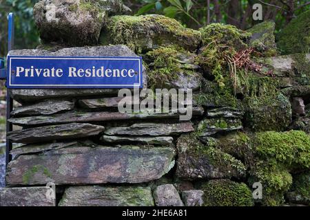 Gedrucktes Schild auf blauem Hintergrund mit der Aufschrift Private Residence an einer alten Steinmauer, die mit Moos und Flechten bedeckt ist Stockfoto