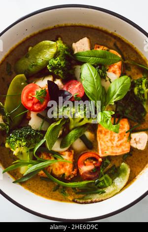 Veganes grünes Thai-Papyrus mit gebratenem seidigen Tofu-Brokkoli und Schneeerbsen, gekrönt mit frisch gepflückten Kräutern aus dem Garten, gesundes pflanzliches Speiserezept Stockfoto