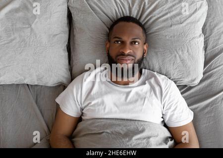 Schwarzer Mann liegt im Bett und denkt nach, Draufsicht Stockfoto