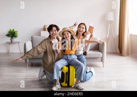 Happy teen Mädchen im Hut halten Flugzeug auf Koffer sitzen, junge asiatische Dame und Mann freuen sich, Spaß haben und Pass zeigen Stockfoto