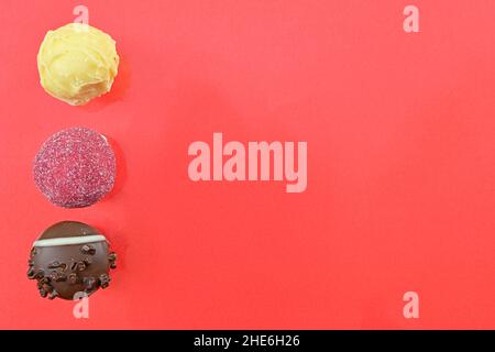 Schokoladenbonbons oder Pralinen auf rotem Hintergrund. Sortiment von Schokoladenpralinen auf rotem Hintergrund mit Kopierfläche. Flach liegend, Draufsicht Stockfoto