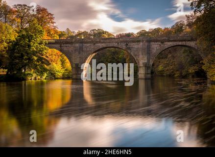 Eine lange Exposition einer schönen Bogenbrücke in der Nähe der Kathedrale von Durham mit den Herbstfarben, die sich im River Wear widerspiegeln Stockfoto