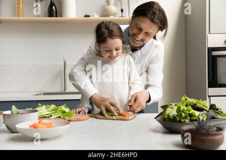 Fröhlicher Vater, der kleine Tochter beibringt, Salat zu kochen Stockfoto