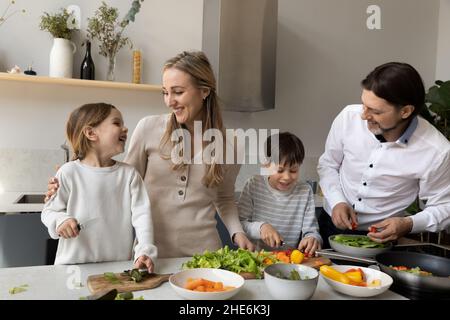 Fröhliche süße Geschwister Kinder helfen Eltern, das Abendessen vorzubereiten Stockfoto