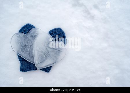 Zwei Herzen - ein Symbol der Liebe, aus Eis, auf warm blau gestrickten Fäustlingen, auf dem Schnee. Valentinstag. Speicherplatz kopieren. Romantisches Konzept. Stockfoto