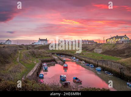 The Burn mit den vertäuten Fischerbooten von Seaton Sluice, Northumberland bei Sonnenaufgang, mit dem feurigen Himmel, der sich im Wasser spiegelt Stockfoto