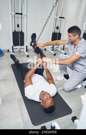 Männlicher Patient, der unter Aufsicht eines Physiotherapeuten eine Kniebeugung macht Stockfoto