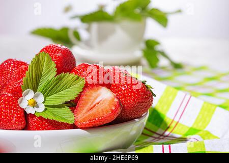 Erdbeeren in weißer Porzellanschüssel auf einem Tisch. Schüssel gefüllt mit saftig frischen reifen roten Erdbeeren. Selektiver Fokus Stockfoto