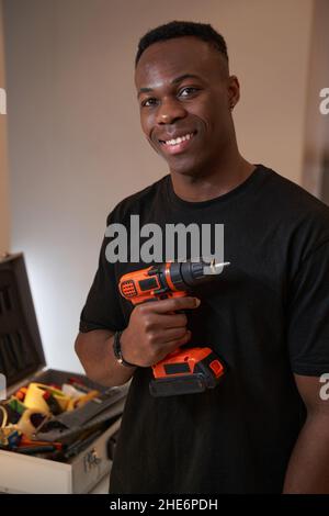 Rüde lächelt zur Kamera, während er die Bohrmaschine hält Stockfoto