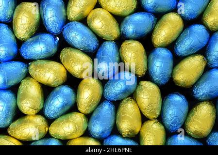 Stapel oder Gruppe von mehrfarbigen und verschiedenen Größen von bunten Folie verpackt Schokolade ostereier in blau, gelb und lindgrün. Stockfoto