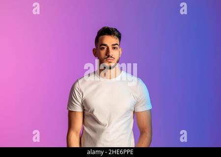 Porträt eines hübschen jungen Mannes aus dem Nahen Osten mit ernstem Gesichtsausdruck und lässiger Kleidung in Neonlicht Stockfoto