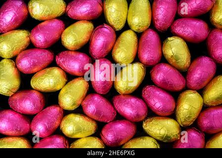 Stapel oder Gruppe von mehrfarbigen und verschiedenen Größen von bunten Folie verpackt Schokolade ostereier in gelb, Gold und rosa. Stockfoto