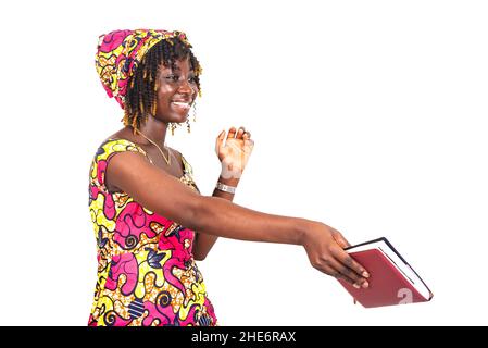 Schöne junge Frau in traditionellem Lendenschurz, die ein Notizbuch gibt, während sie lächelt. Stockfoto