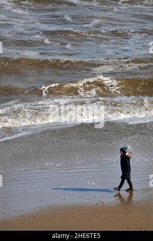 Einsame, sozial distanzierte Frau, die am Ufer des mundesley norfolk england entlang geht Stockfoto