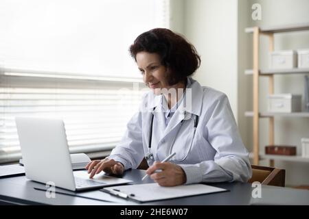 Glückliche alte reife weibliche Ärztin, die im Klinikbüro arbeitet. Stockfoto