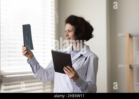Konzentrierter älterer Arzt, der Röntgenbilder in der Klinik untersucht. Stockfoto