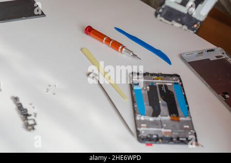 Repair of smartphones concept. Hand tool and disassembled phone lying on the table. Part of a series. Indoors. Selective focus. Stockfoto