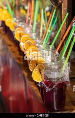 Vordergrund in vertikaler Ansicht einer Reihe von Sangria-Gläsern mit orangefarbenen Scheiben und farbigen Trinkhalmen. Sangria ist ein erfrischendes Getränk aus Spanien Stockfoto