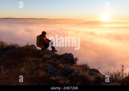 Frau, die am Rand einer Klippe sitzt und einen wunderschönen Blick auf die Landschaft bei Sonnenuntergang am Kraski Rob, oberhalb des Dorfes Crni Kal in Slowenien, genießt Stockfoto