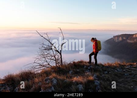 Frau am Rande einer Klippe mit Blick auf eine wunderschöne Landschaft bei Sonnenuntergang in Kraski Rob, über dem Dorf Crni Kal in Slowenien Stockfoto