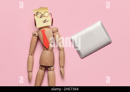 Lustige schlafende Schaufensterpuppe mit kleinem Laptop auf farbigem Hintergrund Stockfoto