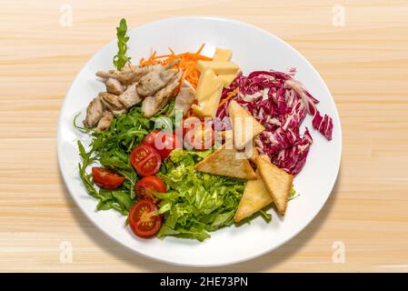 Caesar Salat mit Huhn, Käse, Tomaten und Croutons auf weißem Teller auf Holzboden Stockfoto